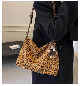 Detail of leopard print tote featuring knotted brown leather strap and plush monster charm
