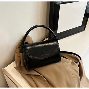 Detail of black patent leather crossbody bag with debossed logo on stylish tan blazer