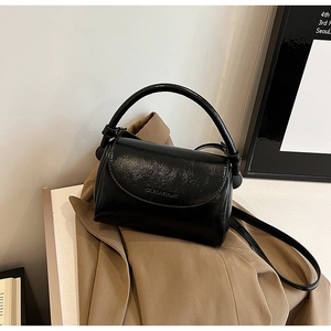 Detailed macro view of black glossy synthetic leather handbag with embossed logo and shoulder strap