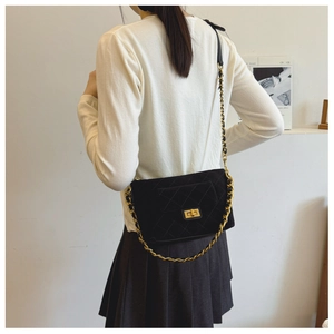 Detail of quilted black suede crossbody bag with gold twist lock and woven chain strap
