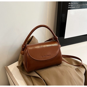 Detail of caramel brown glossy leather handbag with embossed text on khaki fabric
