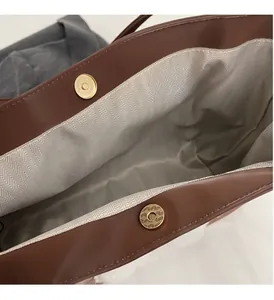 Detail view of large brown tote bag showing herringbone lining and golden magnetic closures