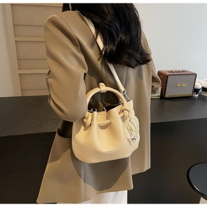 Detail der cremefarbenen Falten-Eimertasche mit Perlenanhänger und rundem Griff im Freien