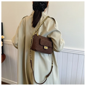 Detail of dark brown quilted crossbody bag with gold chain strap on a beige trench coat