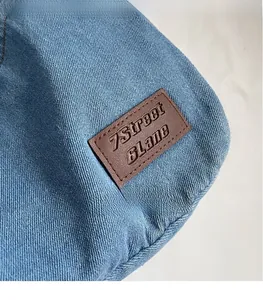 Macro shot of blue denim tote bag with brown leather logo patch and stitched texture