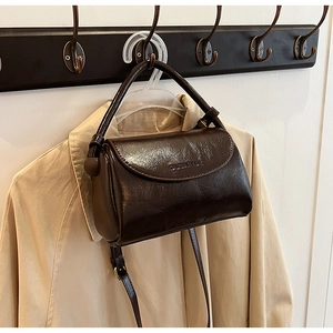 Detail of dark brown vintage square bag hanging on hook beside beige trench coat