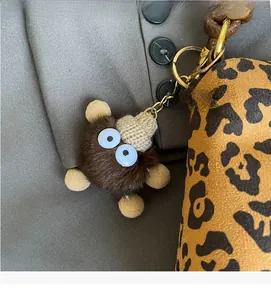 Detail of furry monster bag charm with white eyes and hat on leopard print tote