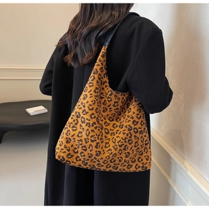 Detail of large leopard print tote bag featuring black leather strap and textured fabric