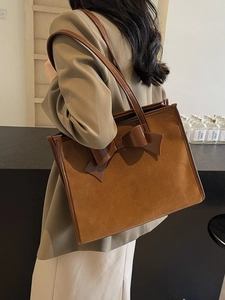 Brown suede tote bag with large leather bow detail worn by a model in casual style