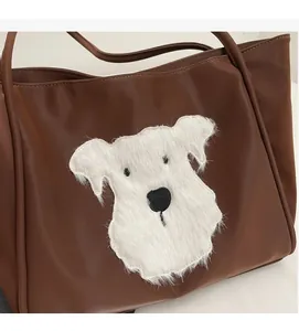 Detail of a dark brown leather tote bag featuring a white plush dog head applique decoration