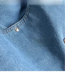 Detail of blue denim tote bag showing twill fabric texture, brown stitching and silver rivet