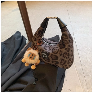 Detail of leopard print crossbody bag featuring a plush bear charm and brand label
