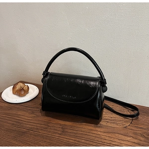 Close-up of black glossy patent leather small square bag with CLEAPSK logo on wood