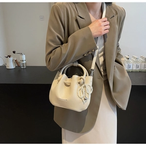 Detail der cremefarbenen Faltenbeuteltasche mit Perlenkette und Herzanhänger am Model