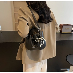 Detail der schwarzen Plissee-Beuteltasche mit Perlenanhänger zu einem beigen Blazer