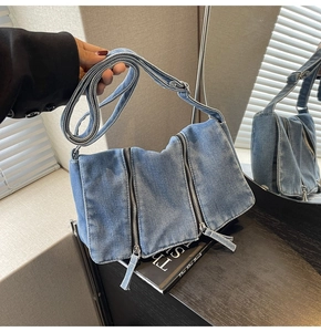 Detail of light blue denim tote bag featuring vertical zippers and long fabric pullers