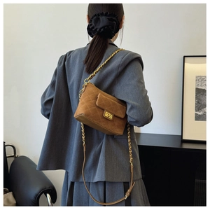 Brown quilted suede crossbody bag with gold chain strap shown on a model in a grey suit