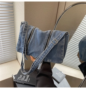 Close-up of blue washed denim tote bag with vertical metal zippers and adjustable strap
