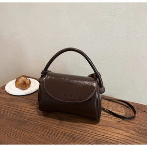 Close-up of a vintage dark brown glossy leather handbag on a rustic wooden table