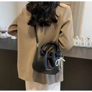 Modische schwarze Leder-Eimertasche mit Perlen-Schleife-Anhänger an einem Model getragen