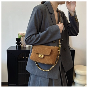 Close-up of quilted dark brown suede handbag with golden chain and metallic twist lock