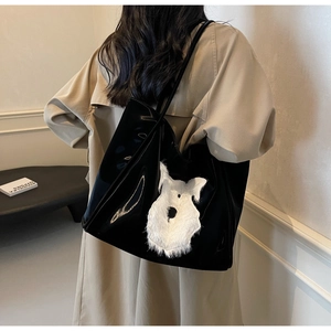 Detail of a black glossy tote bag with white plush animal patch shown on a shoulder