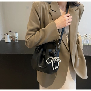 Detail einer schwarzen Leder-Eimertasche mit weißem Perlenbogen-Anhänger und silbernem Herz