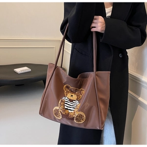 Detail of a brown leather tote bag with a cute bear patch and dual shoulder straps