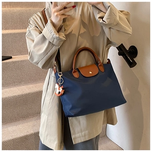 Detail of navy nylon tote bag featuring brown leather handles and decorative horse charm
