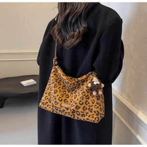 Leopard print tote bag with brown straps and plush charm shown on a model in a black coat