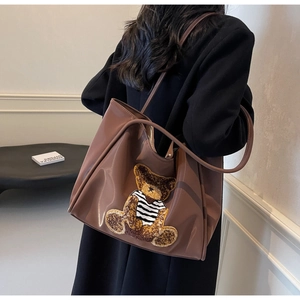 Detail of a large brown glossy tote bag with a 3D plush teddy bear on the side