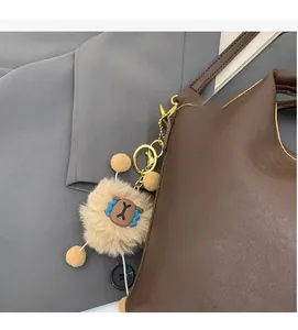 Close-up of fluffy monster pendant with gold keychain on brown leather handbag