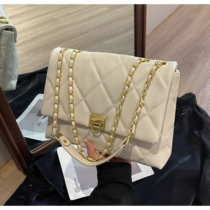 Detailansicht der beigen gesteppten Tasche mit goldenem Drehverschluss und Metallkettenriemen