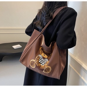 Detail view of large dark brown patent leather tote bag with a cute bear patch