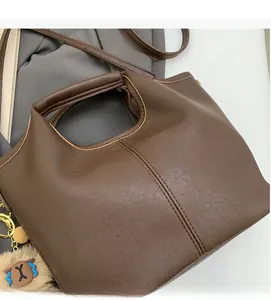 Close-up of brown leather tote bag with lychee grain texture and soft plush bear charm