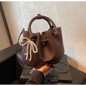 Detail der dunkelbraunen Eimer-Tasche aus Leder mit Perlen-Schleifen-Anhänger
