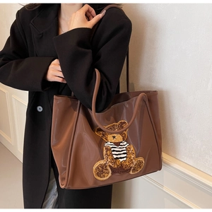 Brown tote bag with bear embroidery shown on a model wearing a black winter coat