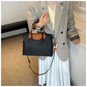 Detail of black nylon tote bag with brown leather handles and a white horse charm