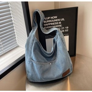 Detail of light blue washed denim tote bag featuring a front pocket and leather brand tag