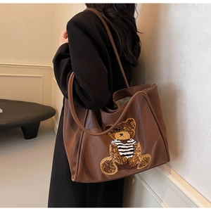 Detail of large brown tote bag with striped bear patch and smooth leather texture