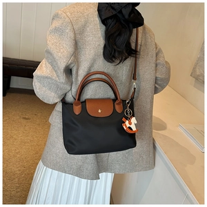 Detail of black nylon tote with brown leather flap, gold buckle, and horse charm