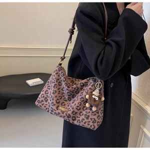 Detail of leopard print tote bag with brown leather straps and plush monster pendant