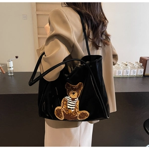 Detail of black glossy tote bag featuring a cute brown teddy bear plush embroidery patch