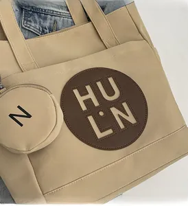 Close-up of beige canvas tote bag featuring hollowed-out logo patch and mini zip coin purse