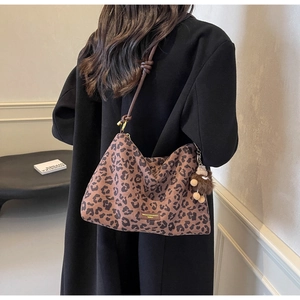 Detail of leopard print tote bag featuring brown leather strap and plush bear charm