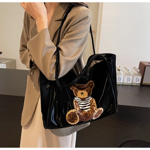 Detail of black glossy tote bag featuring a cute striped bear patch and spacious design