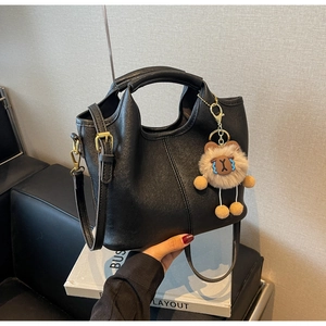 Detail of black faux leather handbag with vertical stitching and cute brown bear charm