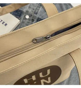 Detail shot of smooth zipper closure on a khaki canvas tote bag with letter patch