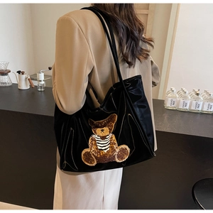 Close-up of a large black tote bag featuring a teddy bear patch in a cafe setting