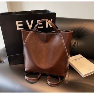 Detail view of brown leather tote bag with white stitching and vertical zippers